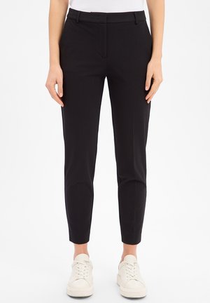 Black fitted trousers made of smooth fabric, featuring a mid-rise waist, belt loops, and ankle-length. Paired with white sneakers.