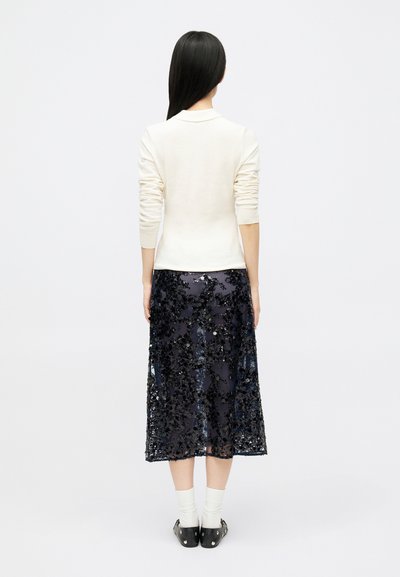 White sweater with fitted sleeves paired with a navy sequined midi skirt. The skirt features a floral pattern and sheer overlay. Black footwear visible.