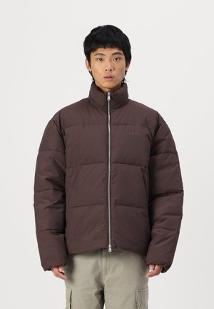 Braune Pufferjacke mit hohem Kragen, Reißverschluss und gesteppter Optik. Verfügt über Seitentaschen und ein dezentes Logo auf der Brust.