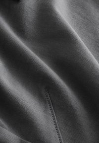 Temno siva tkanina z gladko teksturo, opremljena z nežnimi šivi in drapirano pojavnostjo. Brez vidnih vzorcev ali kovinske opreme.