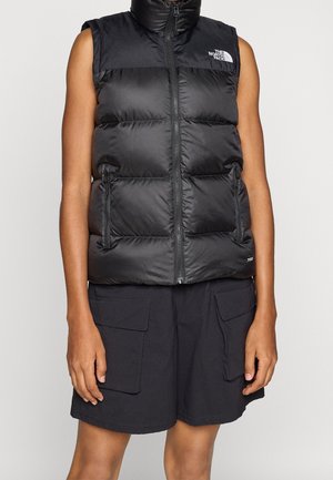 Sleeveless black puffer vest with front zipper and zippered pockets worn over black cargo shorts with flap pockets.