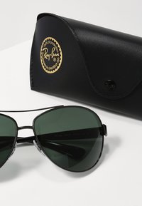Occhiali da sole Ray-Ban aviator con lenti verde scuro, montatura in metallo e nasalini trasparenti. Include un astuccio in pelle nera con logo dorato.