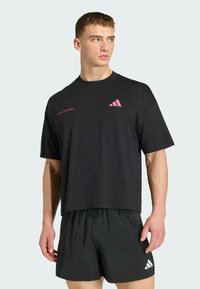 Μαύρο βαμβακερό t-shirt με ροζ λογότυπο Adidas, κοντά μανίκια και άνετη εφαρμογή, συνδυασμένο με μαύρο σορτς από ελαφρύ υλικό.
