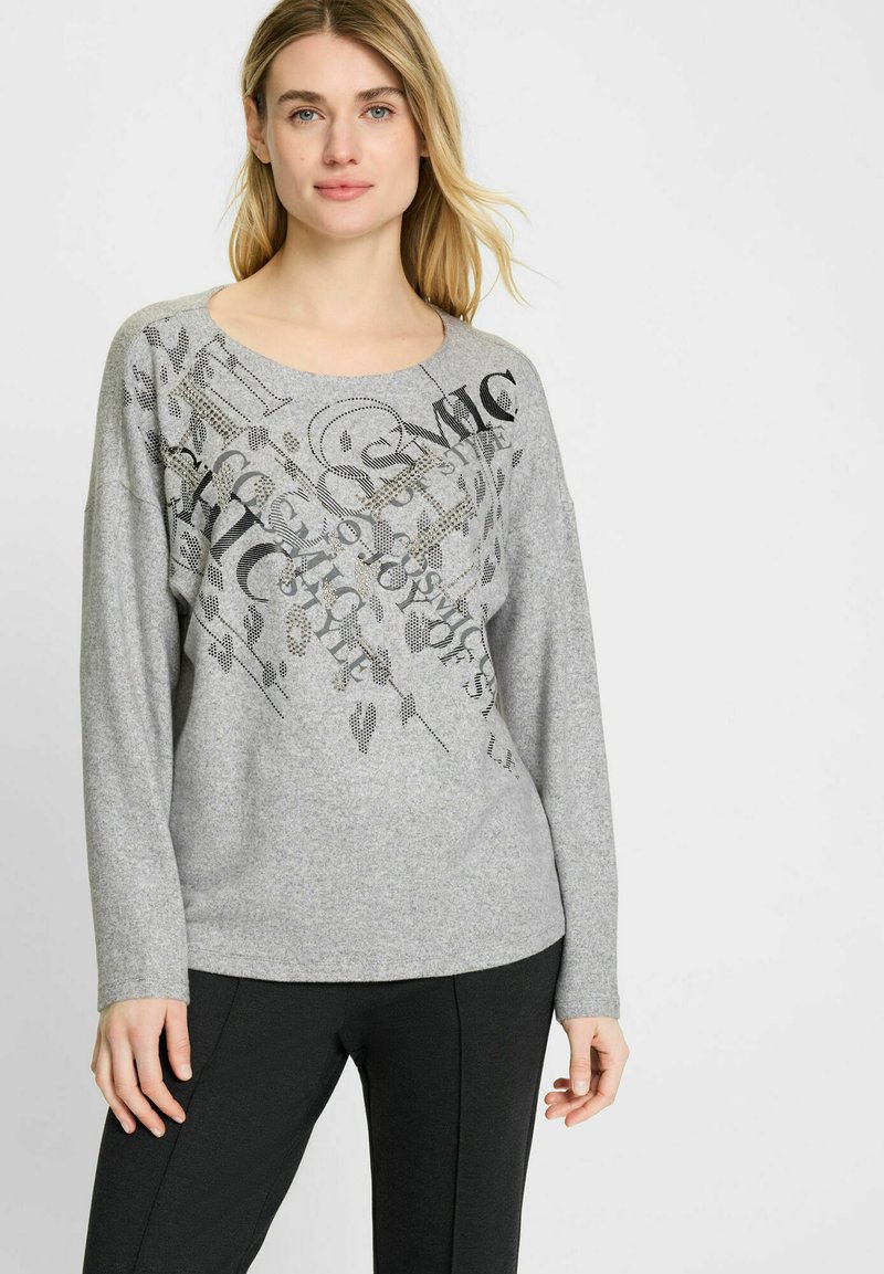 Grijze longsleeve trui met ronde halslijn en een grafische print in zwart. Zachte textuur met een ontspannen pasvorm, gecombineerd met donkere broeken.