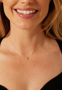 Collier en or avec une chaîne délicate et un petit pendentif en forme de lettre "R". Porté sur une peau nue, présentant une finition lisse.