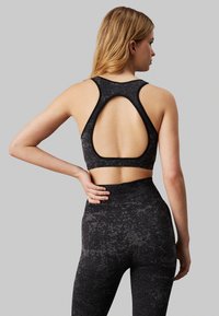 Reggiseno sportivo nero con design aperto sulla schiena, realizzato in tessuto testurizzato. Presenta anche uno stile a schiena scoperta e una cintura liscia.