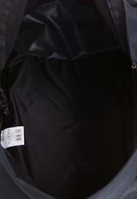 Černý interiér tašky s hladkým látkovým povrchem s mírným leskem. Viditelný zip a štítek s pokyny na levé straně.