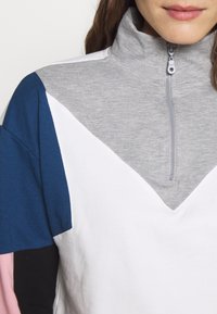 Grauer Zip-Pullover mit einem Farbblockdesign, das blaue, weiße, rosa und schwarze Abschnitte zeigt. Weicher, baumwollartiger Textur.