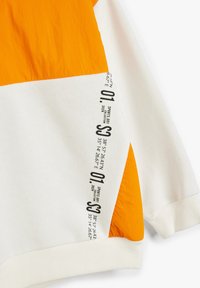Sudadera con bloques de color que presenta paneles naranjas y blancos, puños de canalé y coordenadas impresas con texto negro. Tejido suave y texturizado.