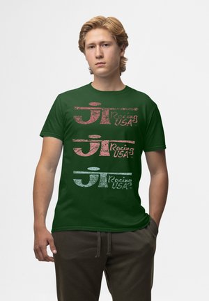 T-shirt en coton vert avec trois logos empilés de couleurs différentes : rouge, rose et bleu, accompagnés du texte "Racing USA" et de styles texturés distincts.