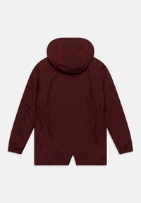 Giacca impermeabile marrone con cappuccio, vita elasticizzata e maniche lunghe. Tessuto morbido con uno spacco sull'orlo posteriore per un movimento maggiore.