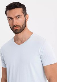 Vaaleansininen puuvillainen V-pääntie t-paita lyhyillä hihoilla, jossa on sileä rakenne ja minimaalinen muotoilu. Ei näkyviä kuvioita tai yksityiskohtia.