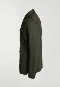 Chemise boutonnée à manches longues vert foncé avec poche à rabat sur la poitrine, col et poignets boutonnés, vue de profil droit sur un fond uni.