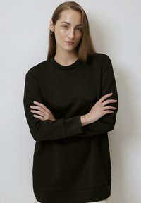 Fekete pulóver kerek nyakkal, hosszú ujjal és laza szabással. Puha anyagból készült, sima textúrával és minimalista dizájnnal.