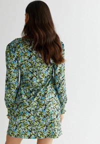 Blommig klänning med långa ärmar, med svart bakgrund prydd med blå och gröna blommor. Slät tyg och avslappnad passform.