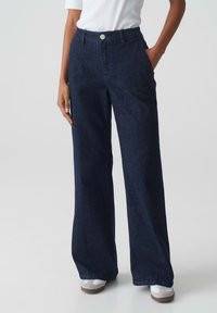 Breed gesneden donkerdenim jeans met een hoge taille, subtiele textuur en een sluiting met een knoop aan de voorkant, gestyled met zijzakken en een nette zoom.