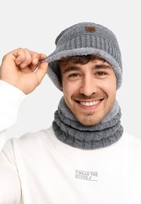 Bonnet gris en tricot avec doublure en polaire et logo cousu, accompagné d'une écharpe grise côtelée assortie. Les deux articles présentent une texture douce.