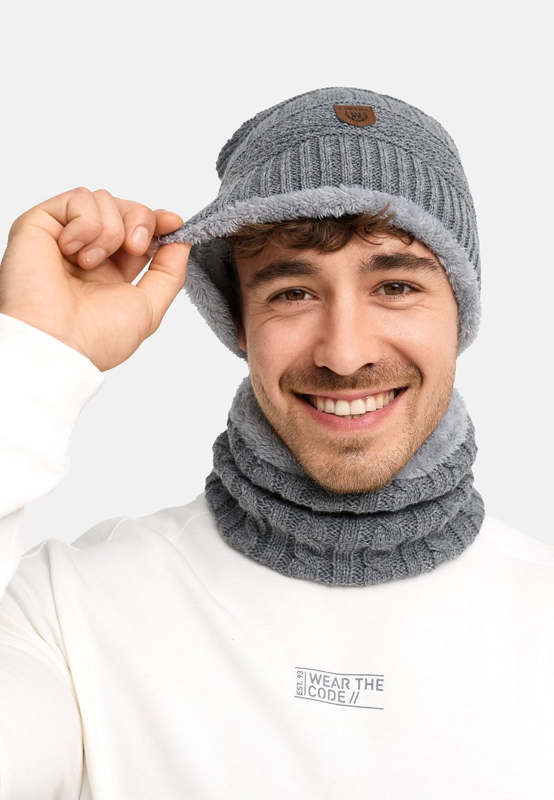 Bonnet gris en tricot avec doublure en polaire et logo cousu, accompagné d'une écharpe grise côtelée assortie. Les deux articles présentent une texture douce.
