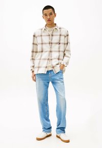 Plaid shirt in cream and brown tones, paired with light blue jeans. White sneakers with brown soles. Simple design with visible stitching.