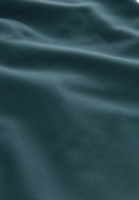 Teal stof met een gladde textuur, met zachte golven en een matte afwerking, die zacht licht en subtiele contouren weerkaatst.