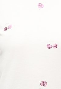 Λευκό ύφασμα διακοσμημένο με μικρές ροζ συστάδες στρας σε σχήμα κερασιών και κουκκίδες διασκορπισμένες σε όλη την επιφάνεια.