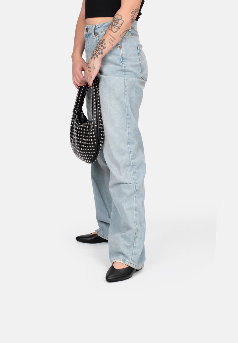 Jeans in denim di un blu chiaro a vita alta, dal fit comodo, abbinati a ballerine nere con punta allungata e a una borsa nera con borchie.