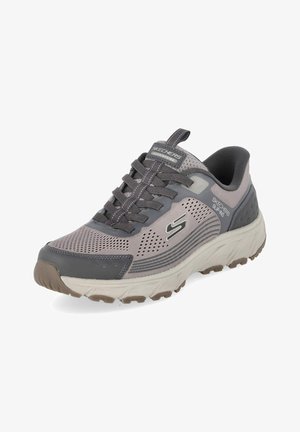 Grauer und beiger Skechers Adventure Slip-On Sneaker mit Mesh-Obermaterial, Schnürdetails und profilierter Gummisohle für den Außeneinsatz.