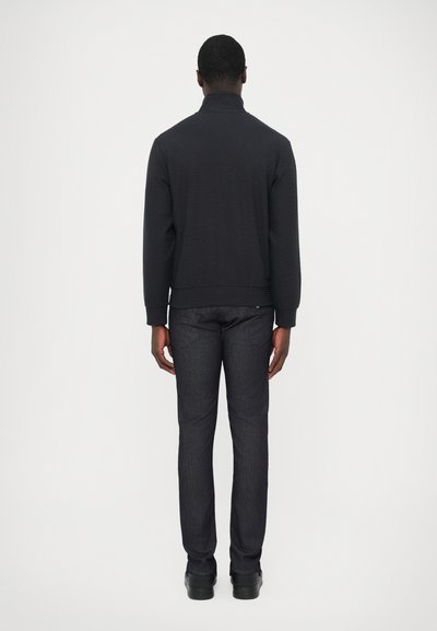 Felpa nera trapuntata con collo alto, abbinata a jeans in denim scuro. L'outfit presenta una vestibilità comoda e una texture liscia.