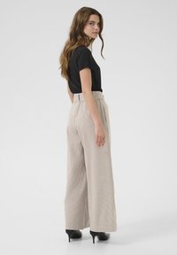 Pantaloni a vita alta, a gamba larga e a righe beige, con un girovita dotato di cintura e una texture sottile, abbinati a una t-shirt nera attillata e tacchi.