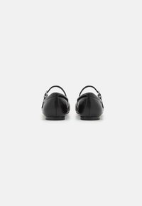 Bailarinas de cuero negro con punta redondeada, tira en el tobillo y tacón bajo, con textura suave y elementos de diseño minimalistas.