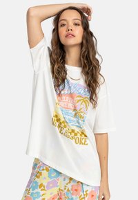 Hvid oversized t-shirt med en farverig strandtema grafik, der har palmer og ternet mønster. Blødt bomuldsstof.