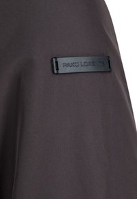Czarna tkanina o gładkiej strukturze z prostokątną metką wytłoczoną z napisem "PAKO LORENTE". Minimalistyczny design podkreśla elegancję materiału.