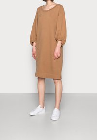 Brun, oversized sweatshirtklänning med rund halsringning och puffärmar. Har en logodetalj och en rak fåll. Bärs med vita sneakers.