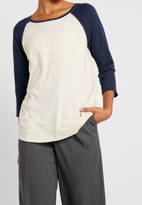 Ljuskrämfärgad t-shirt med trekvartsärmar och marinblå ärmar, rund halsringning, avslappnad passform och mjukt bomullstyg. Inga synliga mönster eller detaljer.