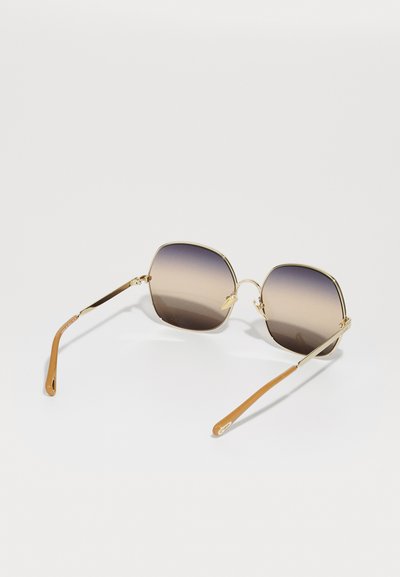 Firkantede solbriller med gradient brune linser, gullfarget metallramme, og brune og beige armer. Har diskré merkevare på armen.