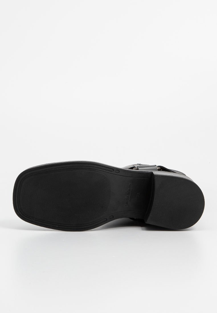 Schwarze Gummisohle mit strukturiertem Grip, ausgestattet mit einer glatten Oberseite und Knöchelriemen zur Unterstützung. Einfaches Design, minimale Akzente.