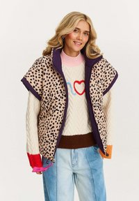 Kamizelka puchowa z beżowym i czarnym wzorem lamparta, z fioletowymi wykończeniami. Noszona na swetrze dzianinowym, z różowym kołnierzem i wzorem w serduszka.