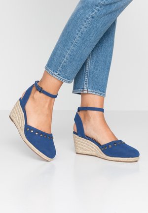Blauwe suède wedge schoenen met een open achterkant, enkelbandje en decoratieve metalen studs langs de teen, met een gevlochten jute zool.