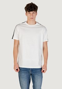 T-shirt bianco in cotone con maniche corte, con accenti neri sulle spalle e un collo rotondo. Indossato con jeans in denim blu.