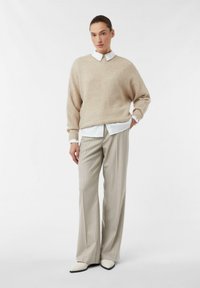 Beżowy prążkowany sweter z dzianiny noszony na białej koszuli z kołnierzykiem, w połączeniu z jasnoszarymi spodniami w prążki i kremowymi, szpiczastymi butami.