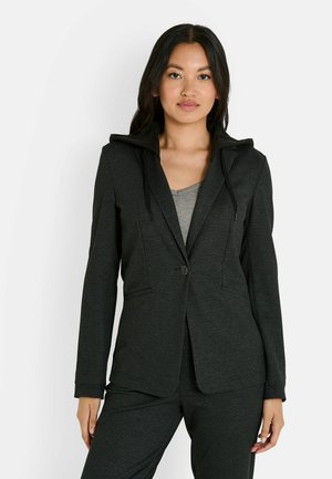 Blazer à carreaux noirs avec capuche et cordons de serrage, présentant une coupe ajustée. Haut gris à col rond visible en dessous.