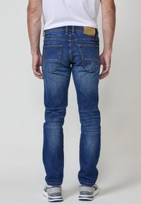 Jeans de mezclilla azul con un corte ajustado, que cuentan con bolsillos traseros con costuras decorativas y un parche de cuero marrón en la cintura.