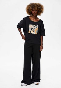 Black oversized T-shirt with an abstract dog graphic, paired with black wide-leg trousers, featuring contrasting side seams and light sneakers.