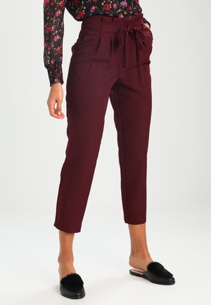 Viininpunaiset räätälöidyt housut, joissa on laskokset ja solmittava vyötärö, valmistettu sileästä kankaasta. Yhdistetty mustiin liukusomakkeisiin, joissa on pörröinen koriste.