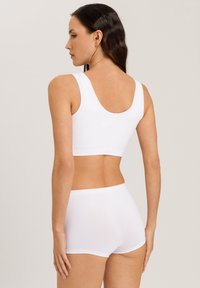Reggiseno sportivo bianco in tessuto con spalline larghe e scollatura bassa, abbinato a pantaloni corti bianchi coordinati, entrambi in un materiale morbido e elastico.
