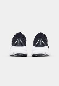 Des chaussures de course noires rembourrées avec une semelle blanche, dotées d'un dessus en mesh lisse, d'un talon renforcé et d'accents réfléchissants sur les côtés.