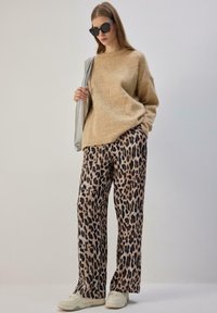 Beež värvi lahtise kudumiga kampsun koos beeži ja musta leopardimustriga laiade püksidega. Modell kannab musti päikeseprille ja valgeid vabaajajalatseid.