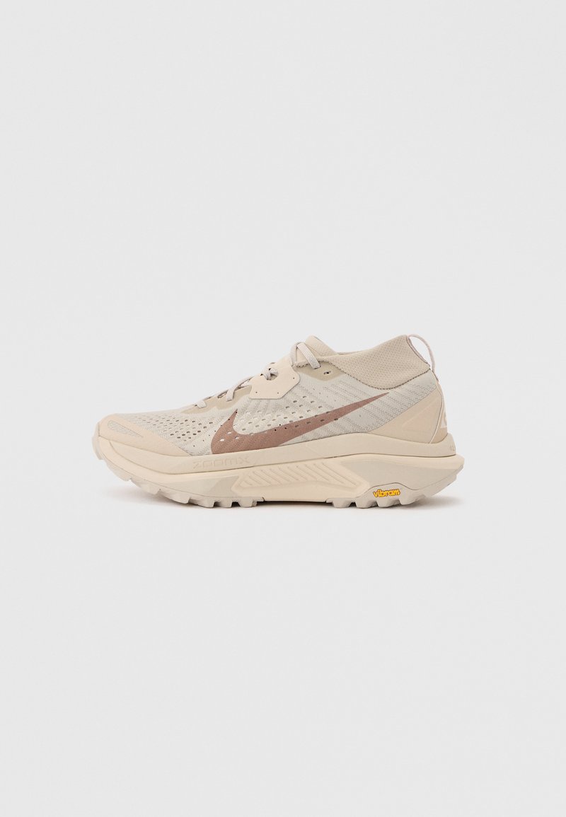 Μπεζ παπούτσι τρεξίματος Nike με καφέ σήμα, αναπνέον δίχτυ, επενδεδυμένο κολάρο και παχιά σόλα Vibram, σχεδιασμένο για ορεινό τρέξιμο.