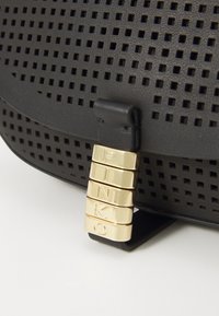 Zwarte geperforeerde leren handtas met een rechthoekige vorm en een gouden sluiting met de naam "PINKO." Textuur met uitsparingen.