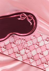 Sovemask med rosa satengsløyfe og blondekant hviler på en mønstret rosa silkeveske på mykt rosa satengstoff.